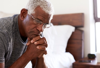 depressed senior man looking unhappy sitting on side of bed