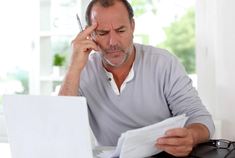 mature man thinking in front of a laptop holding documents