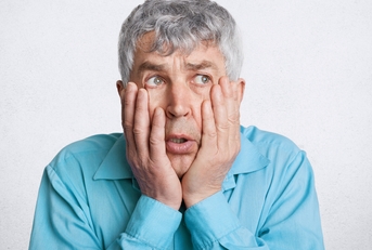 frustrated grey haired male, keeps hands on cheeks
