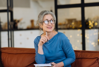 senior woman in glasses thinking and writes in a diary home