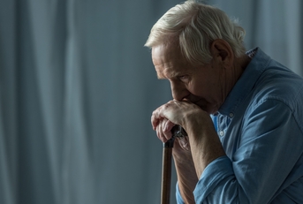 sad senior man leaning on cane in room