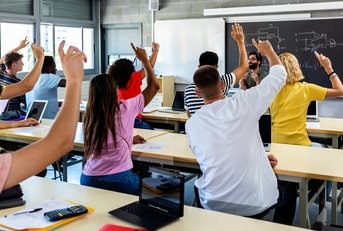 high school students raising hands in classroom