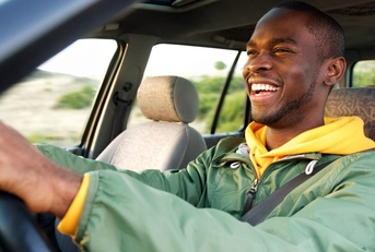 smiling african american man driving car while wearing seatbelt during day time