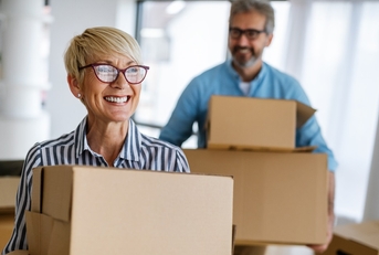 senior couple happily moving into house holding moving boxes