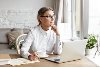 mature female writer sitting at desk at home placing chin on her hands