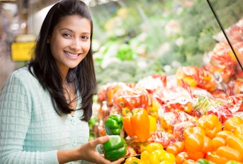 happy woman standing in grocery store buying bell peppers