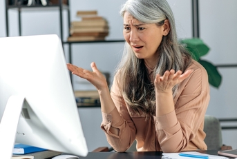 annoyed mature woman looks at computer in confusion