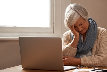elderly woman sitting in front of her laptop looking stressed