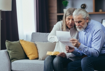 senior husband showing banking paper to confused elderly wife