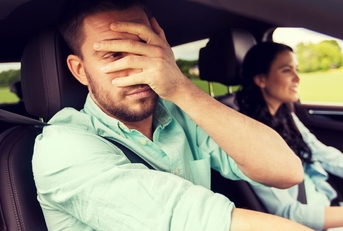 A man in the passenger seat of a car covers his face with his hand. 