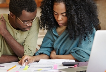 african american couple sitting on table in front of laptop reviewing documents