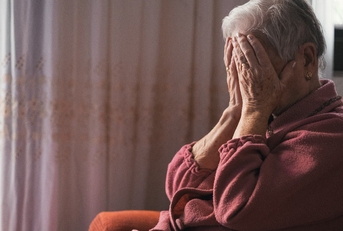 senior lady in depression sitting on couch at home covering her face with hands