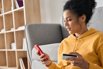 woman wearing yellow hoodie sitting on floor holding card to make payment using smartphone