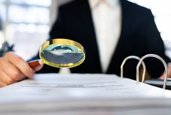 male auditor in suit using magnifying glass to check irs tax audit file on table