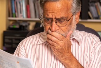 senior man looking at utility bills and covering face in terror
