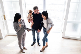 female real estate agent holding papers on clipboard showing new house to couple with baby