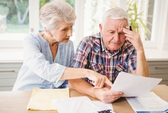 senior couple sitting at table reviewing taxes while doing calculations 