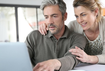 attractive senior couple reviewing financial budget using laptop with papers and cup on table