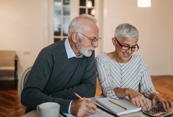 senior couple sitting at wooden table with papers and calculator sorting finances at home for vacation