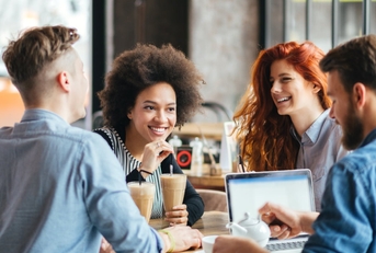 multi ethnic friends sitting at table in cafe talking to each other while drinking coffee and pouring tea in cup