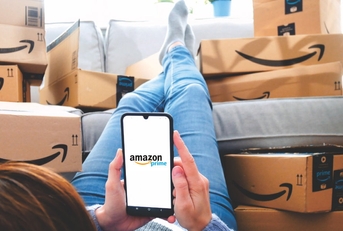 woman using smartphone relaxing in her room while surrounded by Amazon Prime delivery boxes