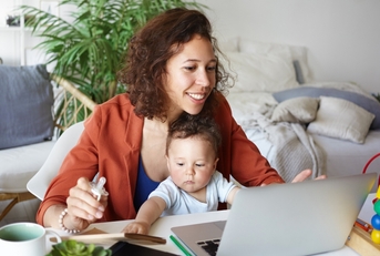 Woman holding baby looking at laptop