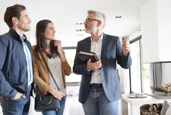 senior real estate agent showing around new modern house to young couple