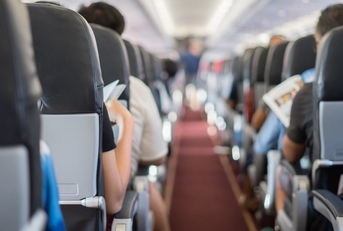 The aisle of an airplane. Passengers fill the seats. 