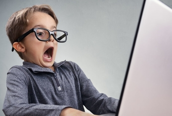 cute boy wearing fake glasses shocked and surprised while using laptop