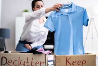 Woman sorting wardrobe into brown boxes with &quot;declutter&quot; and &quot;keep&quot; labels.