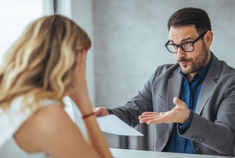 businessman holding papers arguing with young business woman at office