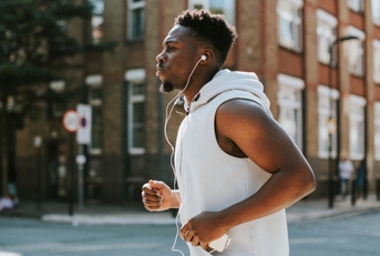 african american man wearing wireless headphones running in street during day time