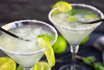 Two margaritas with straws and lime wedges on the rim.