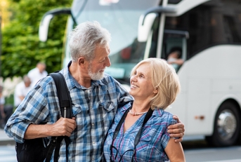 happy senior couple hugging each other on road with tourist bus in background