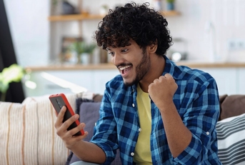 A man looks happy and pumps his fist while looking at his phone. 