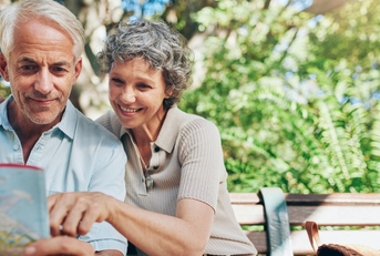 senior couple looking at map in hand while sitting on bench 