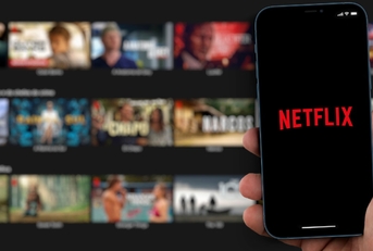 netflix logo on smartphone in man hand with movies in background