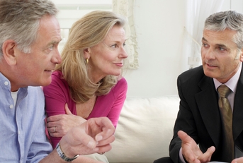 senior couple sitting on sofa with male financial advisor discussing documents