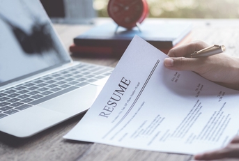 man sitting on table holding pen while reviewing resume at work