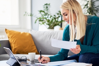 woman sitting on couch at home writing on papers to file tax