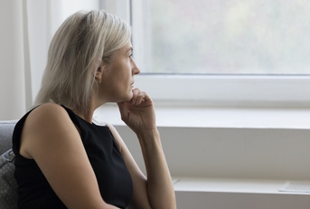 An older woman looks out the window in her home