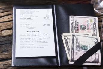 A restaurant bill with a cash tip set to the side. 