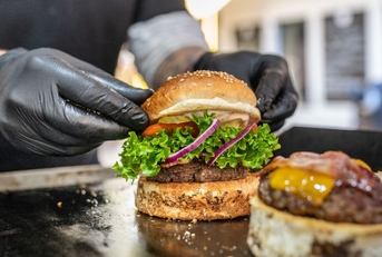 chef wearing black disposable gloves preparing fresh burgers on grill.