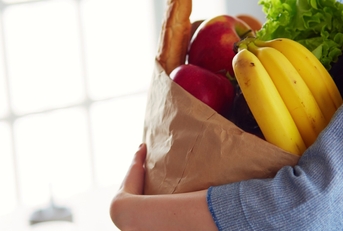 woman holding brown grocery bag with vegetables and fruits