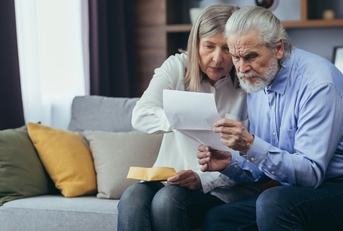 frustrated senior couple sitting on couch at home reviewing bills and taxes