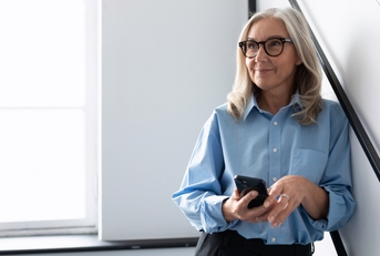 senior business woman standing on stairs at workplace while holding smartphone in hand
