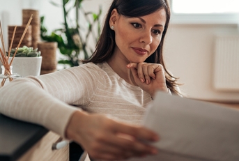 mature woman sitting on couch at home reviewing bills 