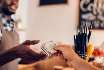 Smiling african american barista taking cash payment from customer on bar counter in cafe.