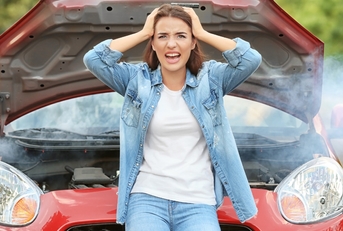 worried young girl holding her head in hands is standing infront of her red car that got out of order.