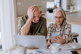 Stressed senior couple calculate expenses or planning budget together while sitting on the table with documents and laptop at home.
